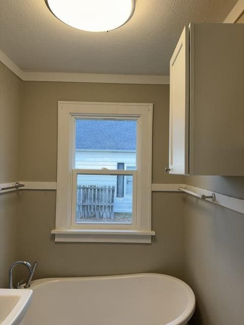 bathroom with a textured ceiling, ornamental molding, and a tub