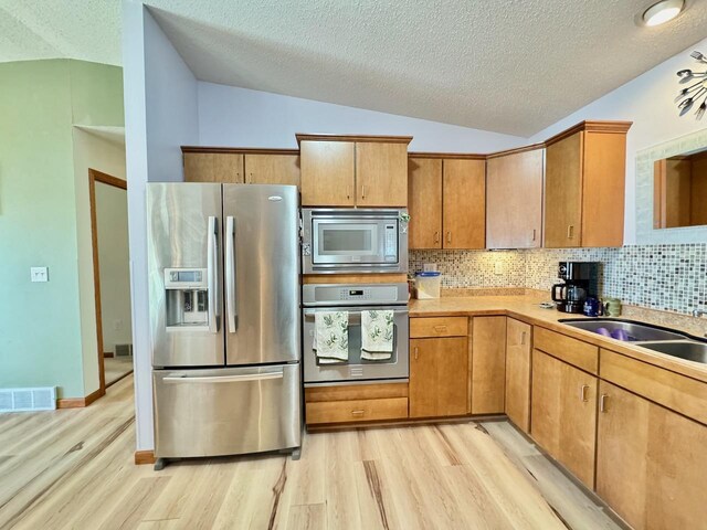 kitchen featuring light hardwood / wood-style floors, lofted ceiling, backsplash, and appliances with stainless steel finishes