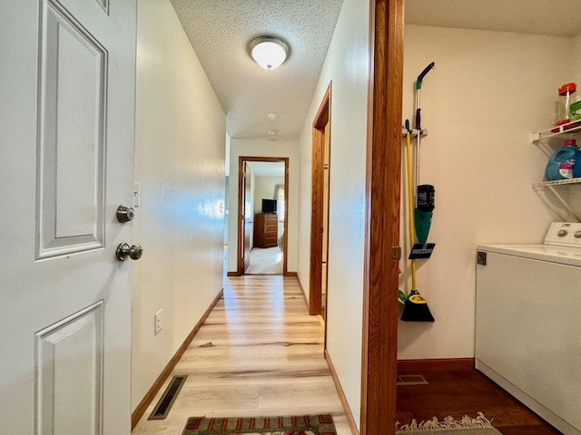 hall with washer / dryer, light wood-type flooring, and a textured ceiling