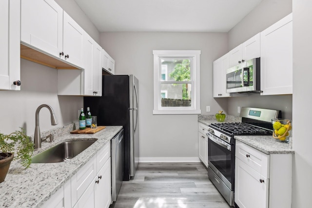 kitchen with light stone countertops, stainless steel appliances, sink, light hardwood / wood-style flooring, and white cabinets