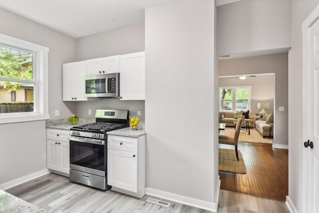 kitchen with white cabinets, a wealth of natural light, stainless steel appliances, and light stone countertops