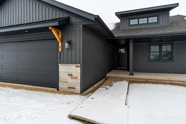 snow covered property entrance featuring stone siding, a porch, board and batten siding, and roof with shingles