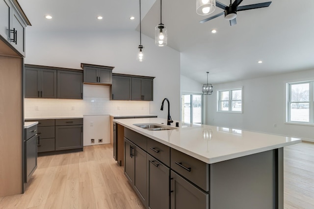 kitchen featuring a sink, a ceiling fan, light wood-type flooring, a center island with sink, and decorative light fixtures