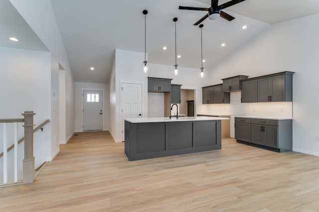 kitchen with high vaulted ceiling, light wood-style floors, hanging light fixtures, decorative backsplash, and a center island with sink