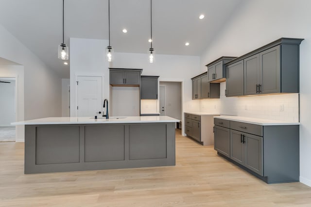 kitchen featuring light wood-type flooring, decorative backsplash, a sink, and a large island with sink