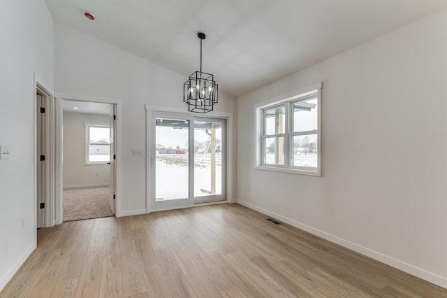 unfurnished dining area with baseboards, visible vents, lofted ceiling, light wood-style floors, and a notable chandelier