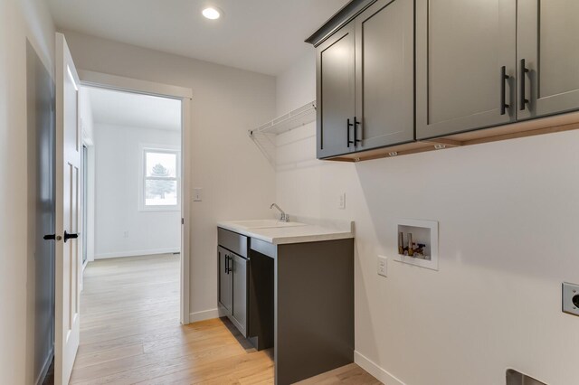 laundry room featuring cabinet space, hookup for a washing machine, hookup for an electric dryer, light wood-style floors, and a sink