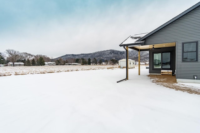 yard covered in snow featuring entry steps, a shed, an outdoor structure, and a mountain view