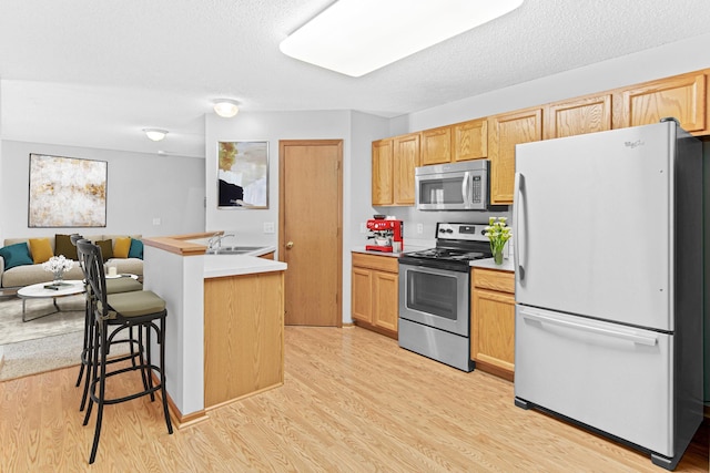 kitchen with appliances with stainless steel finishes, light brown cabinetry, a kitchen breakfast bar, sink, and light hardwood / wood-style floors