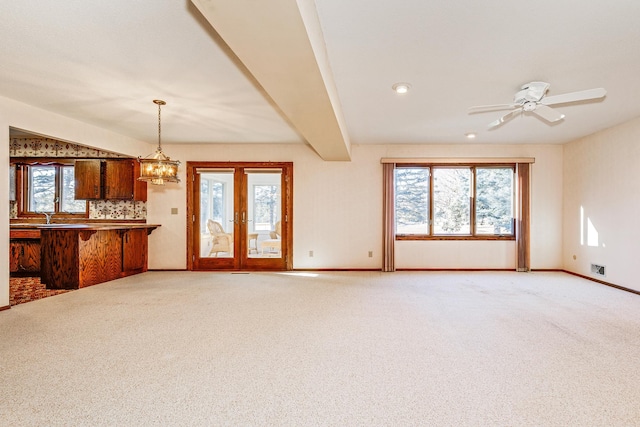 unfurnished living room featuring ceiling fan with notable chandelier and light colored carpet