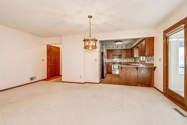 kitchen with light colored carpet, stainless steel appliances, decorative light fixtures, and kitchen peninsula