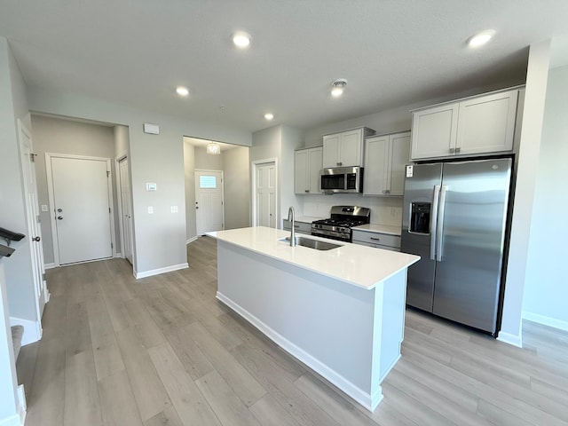 kitchen with a kitchen island with sink, sink, stainless steel appliances, and light hardwood / wood-style floors