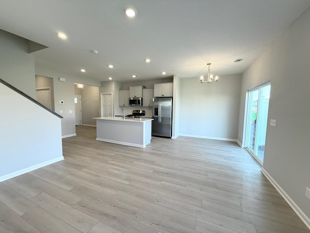 kitchen with white cabinets, light hardwood / wood-style flooring, an island with sink, appliances with stainless steel finishes, and decorative light fixtures