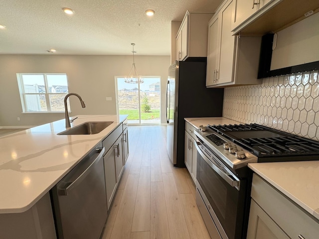 kitchen with appliances with stainless steel finishes, backsplash, sink, pendant lighting, and an inviting chandelier