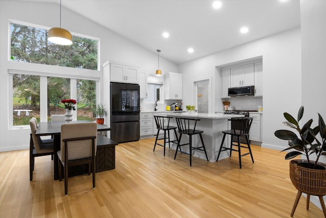 kitchen with decorative backsplash, black refrigerator, white cabinets, and pendant lighting