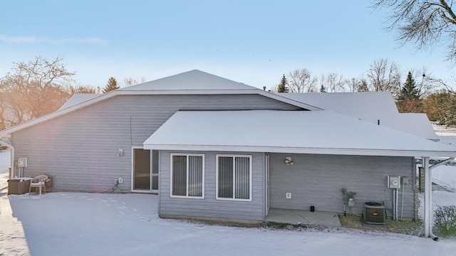 snow covered back of property featuring central AC unit