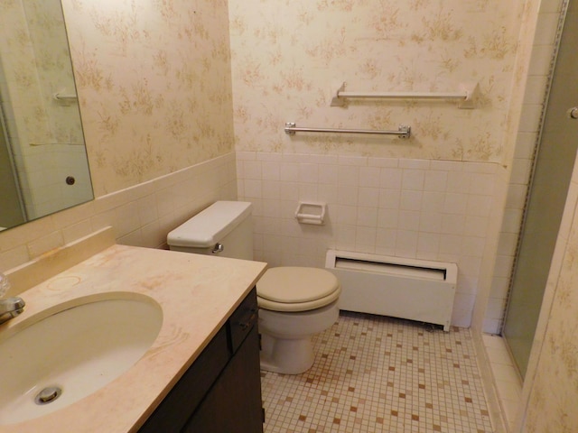 bathroom featuring tile patterned floors, toilet, a shower with door, vanity, and tile walls