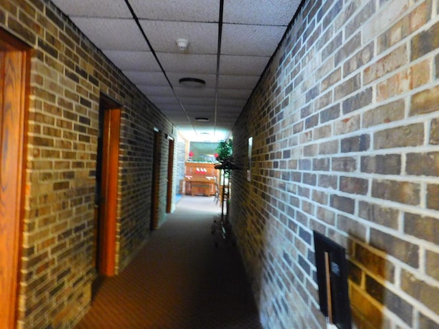 hallway with a paneled ceiling and brick wall