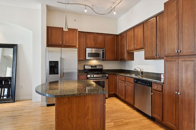 kitchen with light wood-type flooring, stainless steel appliances, sink, a center island, and hanging light fixtures