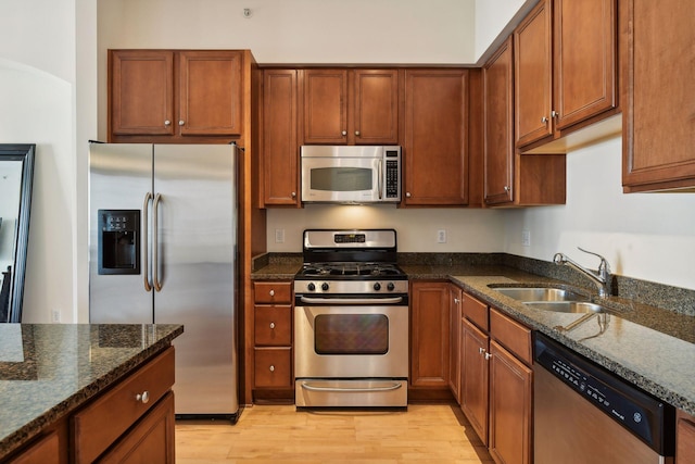 kitchen featuring light hardwood / wood-style floors, sink, dark stone counters, and appliances with stainless steel finishes