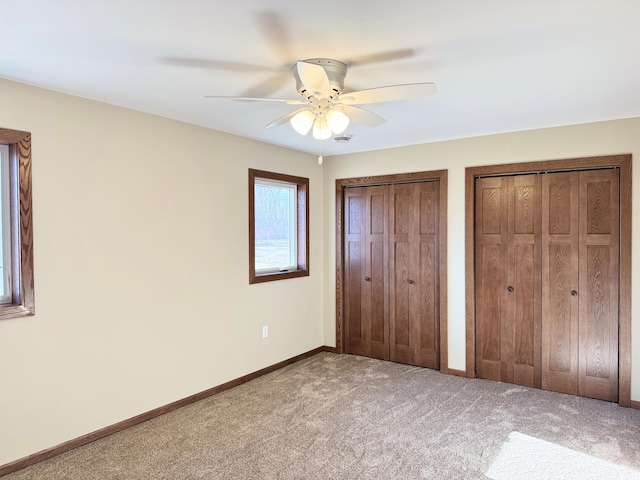 unfurnished bedroom featuring carpet floors, ceiling fan, and multiple closets