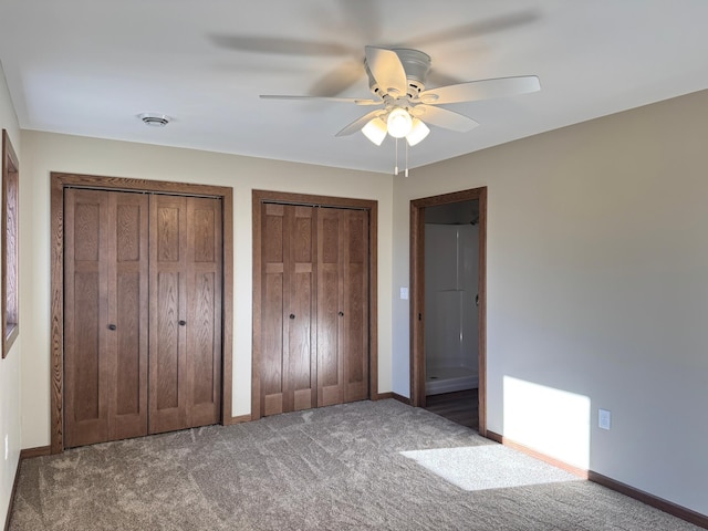 unfurnished bedroom featuring ceiling fan, dark carpet, and multiple closets