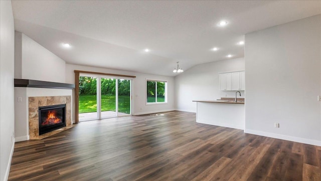 unfurnished living room featuring lofted ceiling, an inviting chandelier, a fireplace, and dark hardwood / wood-style flooring