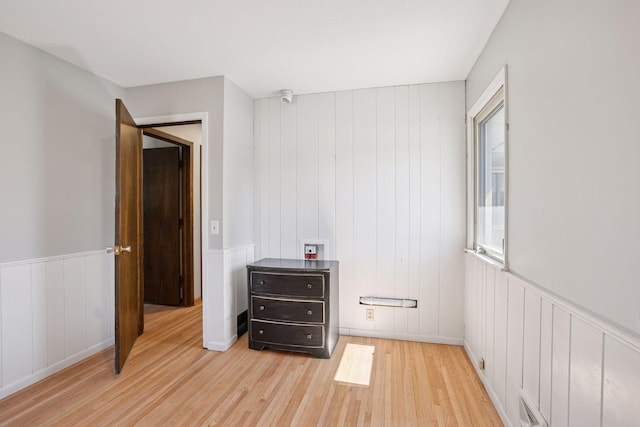 bedroom with light wood-style flooring, a wainscoted wall, and a decorative wall