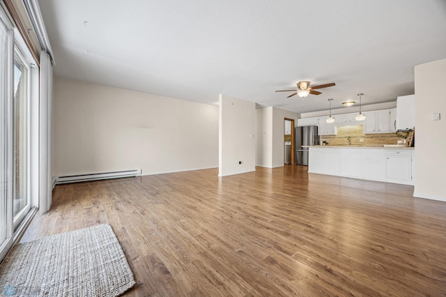 unfurnished living room with hardwood / wood-style flooring, baseboard heating, and ceiling fan