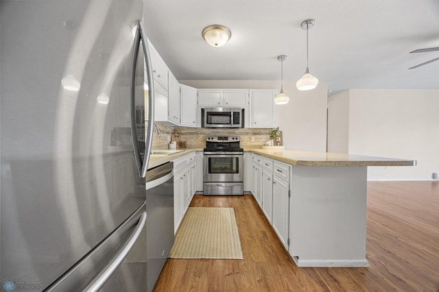 kitchen featuring kitchen peninsula, decorative backsplash, appliances with stainless steel finishes, decorative light fixtures, and white cabinetry