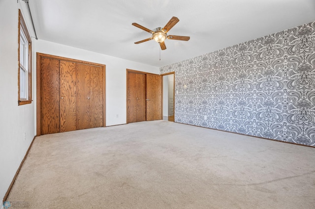 unfurnished bedroom featuring carpet flooring, ceiling fan, and multiple closets