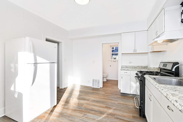 kitchen featuring gas range, light stone countertops, white refrigerator, light hardwood / wood-style floors, and white cabinets