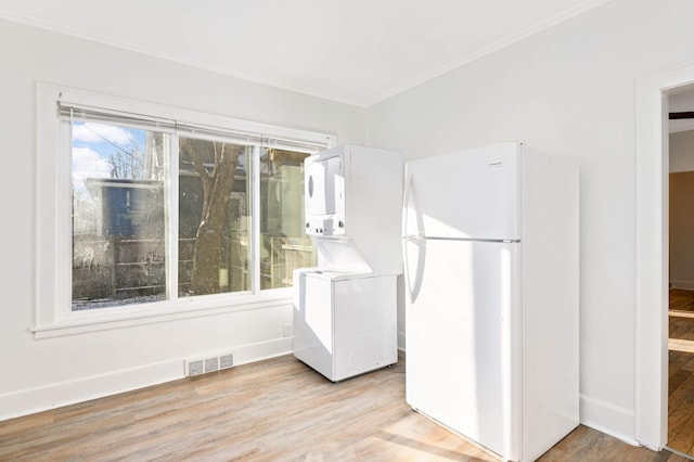 kitchen featuring light wood-type flooring, ornamental molding, white refrigerator, white cabinets, and stacked washer / drying machine