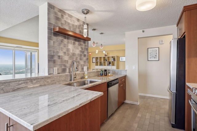 kitchen with sink, stainless steel appliances, hanging light fixtures, light stone counters, and kitchen peninsula