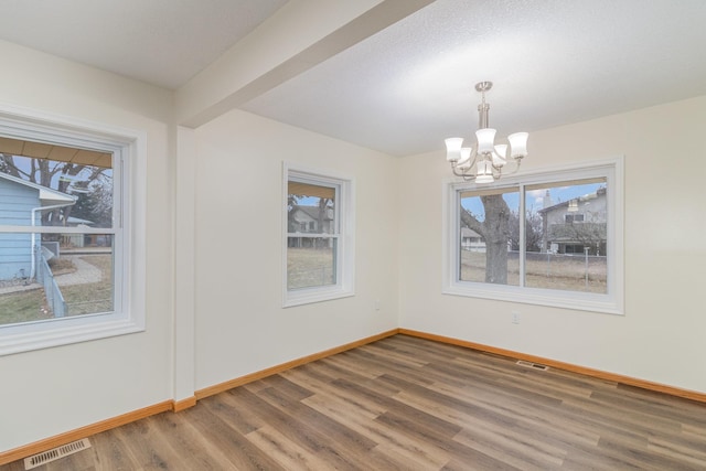 unfurnished dining area featuring beam ceiling, a wealth of natural light, dark hardwood / wood-style flooring, and a chandelier