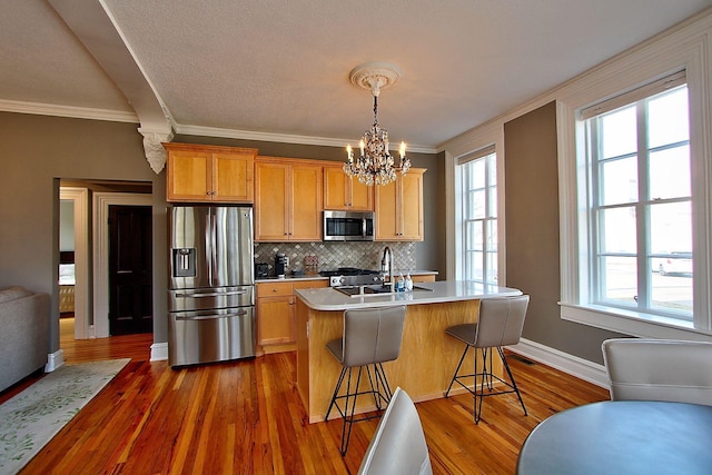 kitchen with a breakfast bar, appliances with stainless steel finishes, crown molding, and an island with sink