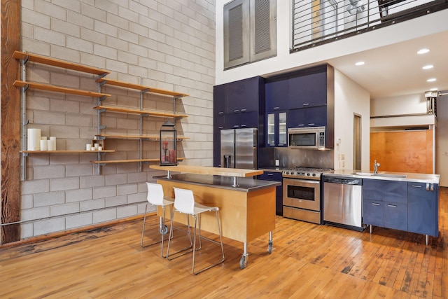 kitchen featuring a kitchen breakfast bar, blue cabinets, a towering ceiling, appliances with stainless steel finishes, and stainless steel counters