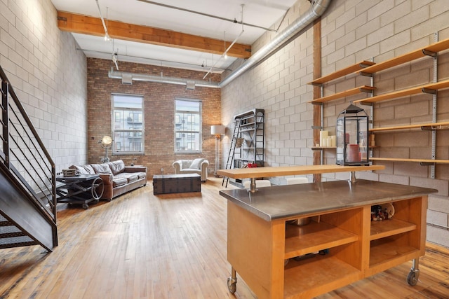 kitchen with beamed ceiling, a high ceiling, light hardwood / wood-style flooring, and brick wall