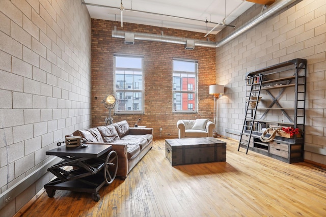 living room with wood-type flooring, a towering ceiling, and brick wall