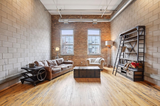 living room with a high ceiling, light wood-type flooring, and brick wall