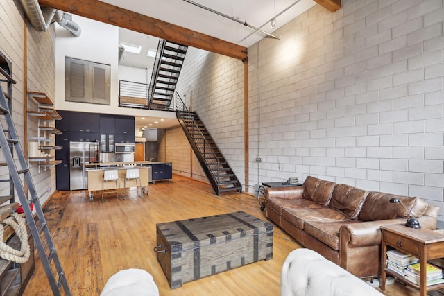 living room featuring beamed ceiling, brick wall, hardwood / wood-style floors, and a high ceiling