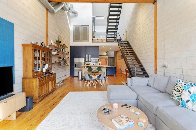 living room featuring light wood-type flooring, brick wall, and a high ceiling