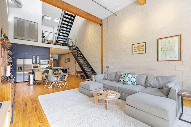 living room with beamed ceiling, brick wall, a towering ceiling, and hardwood / wood-style floors