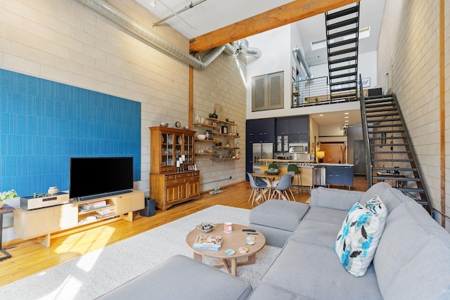 living room with beamed ceiling, brick wall, hardwood / wood-style floors, and a high ceiling