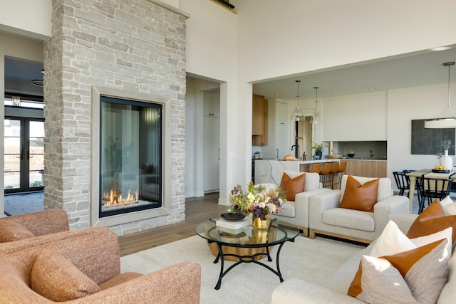 living room with a stone fireplace, light hardwood / wood-style flooring, a high ceiling, and french doors