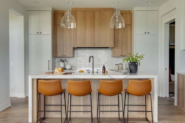 kitchen featuring light stone countertops, light hardwood / wood-style flooring, an island with sink, and tasteful backsplash