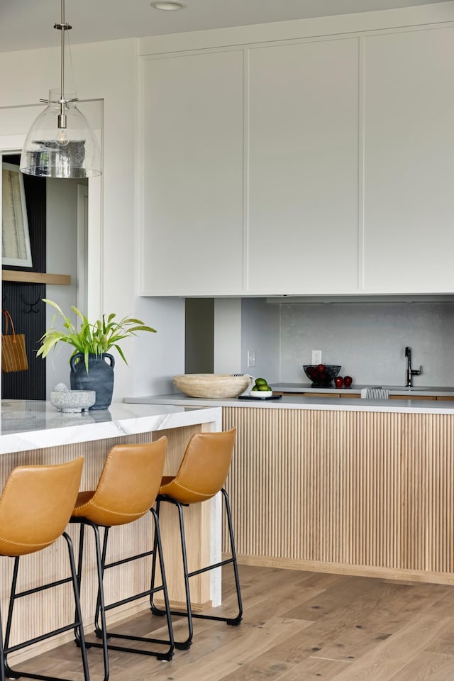 kitchen with backsplash, light hardwood / wood-style floors, a breakfast bar area, and hanging light fixtures