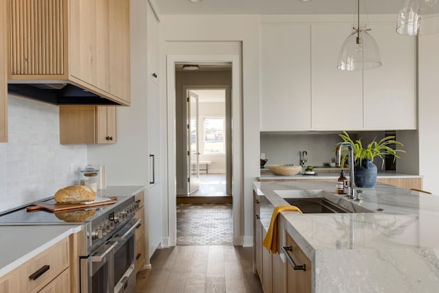 kitchen featuring high end range, sink, decorative light fixtures, hardwood / wood-style flooring, and white cabinets