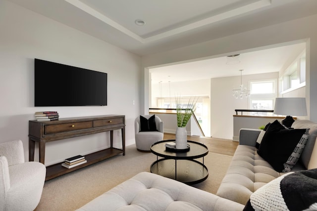 living room featuring a raised ceiling, light wood-type flooring, and an inviting chandelier