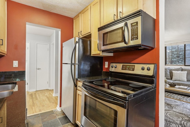 kitchen with light brown cabinets, stainless steel appliances, a textured ceiling, and sink